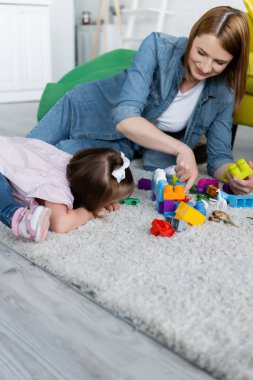 toddler girl with down syndrome playing with happy kindergarten teacher on carpet  clipart