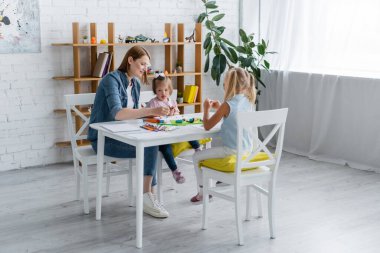 Anaokulu öğretmeni engelli çocuk ve anaokulu kızıyla plastik kalıplar döküyor. 