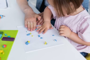 kindergarten teacher molding plasticine with disabled child  clipart