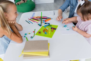 Anaokulu öğretmeni, engelli, Down sendromlu çocukla, mutlu anaokulu çocuğunun yanında plastik kalıplar döküyor. 