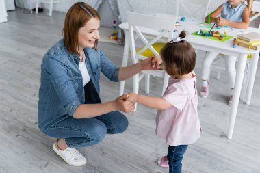 Anaokulundaki mutlu öğretmen, anaokulundaki kızın yanında engelli bir çocukla el ele tutuşuyor.