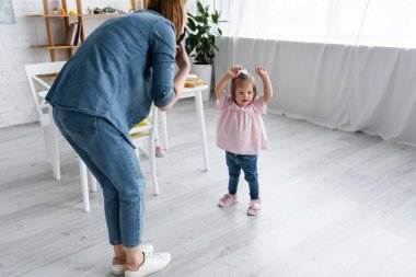 Anaokulu öğretmeni, elleri havada engelli bir çocuğun yanında duruyor.