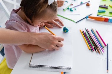 teacher assisting disabled girl with down syndrome drawing in private kindergarten  clipart