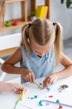 blonde preschooler girl molding molding plasticine in private kindergarten  clipart