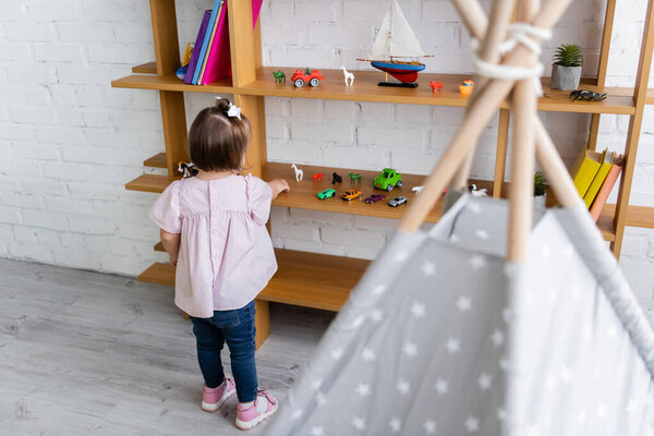 Вид сзади маленькой девочки с синдромом пуха, достигающей игрушек на деревянных рубашках 