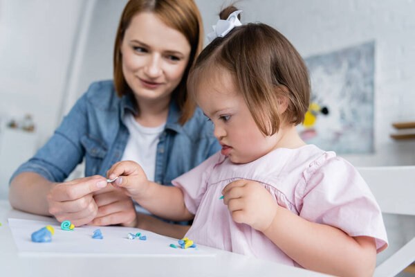 blurred kindergarten teacher molding plasticine with disabled kid with down syndrome 