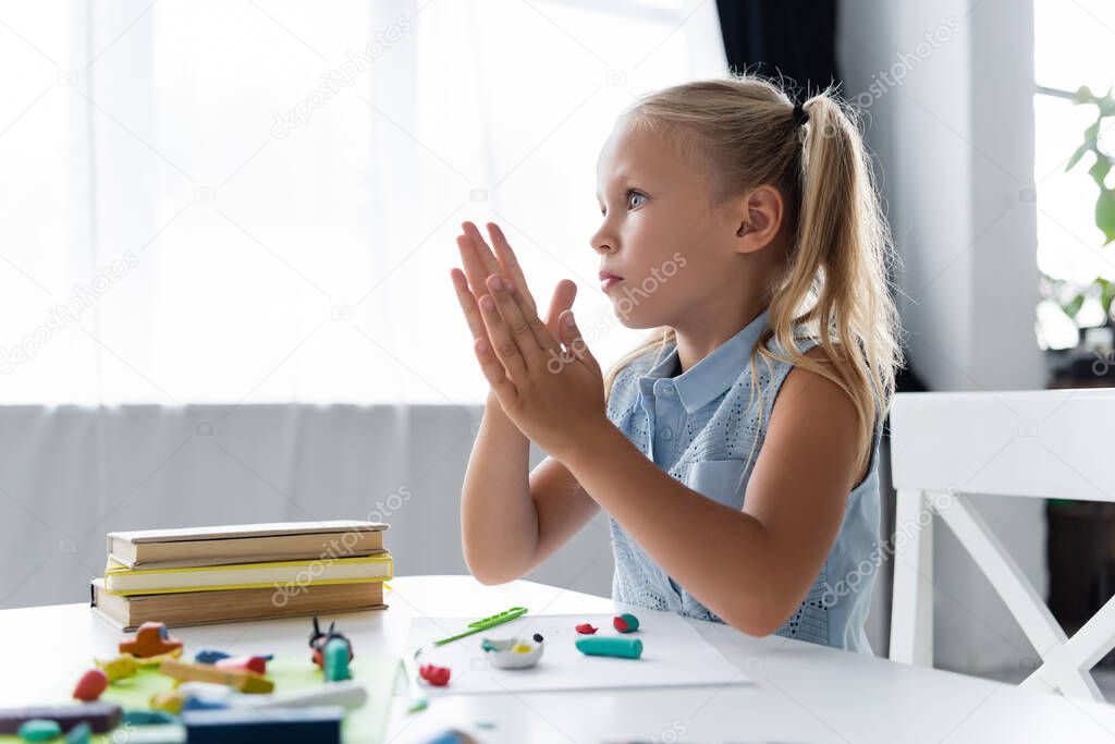 blonde preschooler girl molding plasticine in private kindergarten 