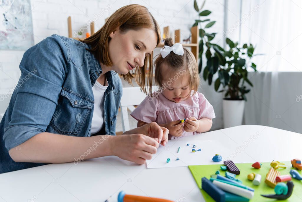 kindergarten teacher molding plasticine with disabled kid with down syndrome 