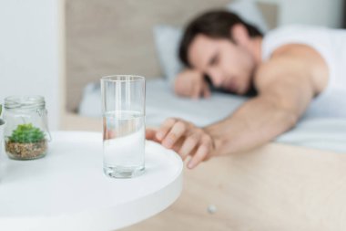 blurred man reaching glass of water while lying in bed clipart