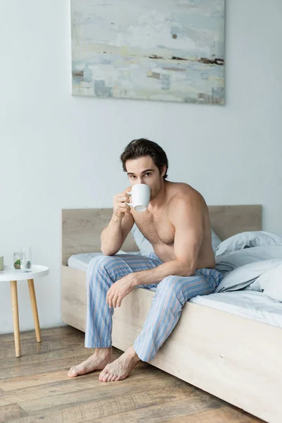 줄무늬 파자마 바지를 셔츠를 침실에서 커피를 마시면서 카메라를 — 스톡 사진