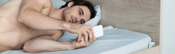 若い無口な男がベッドの上で携帯電話を使って — ストック写真