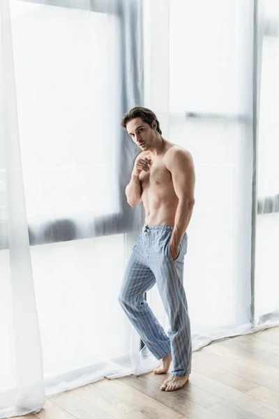 家の窓の近くの青いパジャマパンツの男の完全な長さのビュー — ストック写真