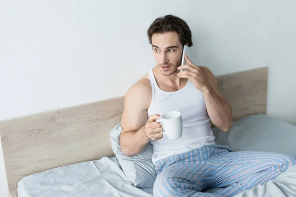 Jovem Falando Telefone Celular Enquanto Sentado Cama Com Xícara Café — Fotografia de Stock