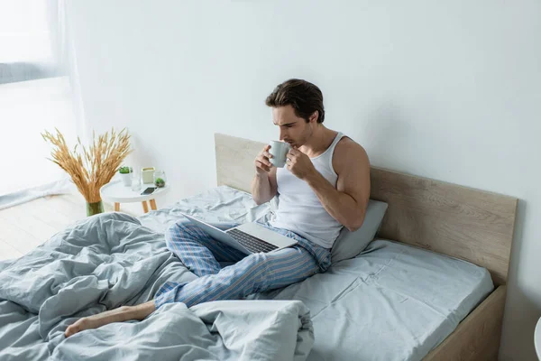 Joven Mirando Computadora Portátil Mientras Bebe Café Cama — Foto de Stock