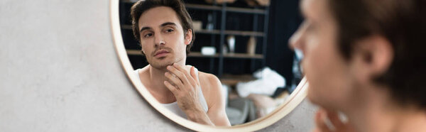 небритый человек трогает щетину на лице у зеркала, знамя