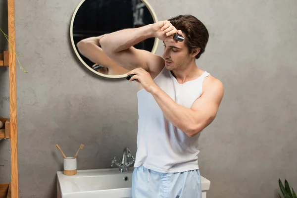 ブルネット男でホワイトタンクトップ適用消臭剤オンArmpitでバスルーム — ストック写真