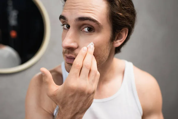 Joven Hombre Aplicando Crema Facial Mientras Mira Cámara —  Fotos de Stock