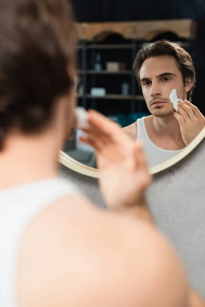 Brunette Man Applying Face Cream Mirror Blurred Foreground — Stock Photo, Image
