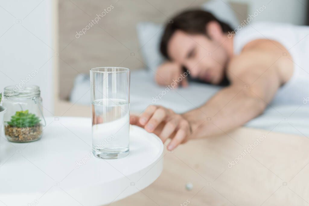 blurred man reaching glass of water while lying in bed