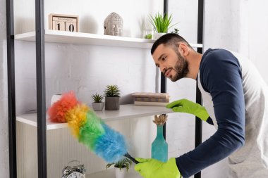 Lastik eldivenli genç adam toz fırçasıyla dolabı temizliyor.