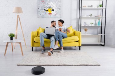 Gülümseyen çok ırklı bir çift evde robot elektrikli süpürge kullanıyordu. 