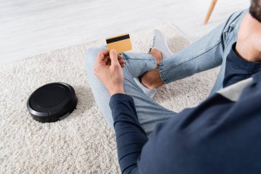 Robotik elektrik süpürgesinin yanında kredi kartı tutan adamın görüntüsü. 