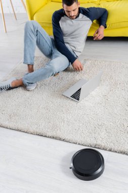 Arka planda dizüstü bilgisayar kullanan robotik elektrik süpürgesinin ve serbest çalışanın yüksek açılı görüntüsü 
