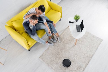 Gülümseyen Afrikalı Amerikalı kadının erkek arkadaşının yanındaki robot elektrikli süpürgeyi göstermesi. 