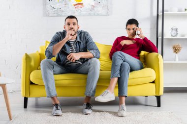 Odaklanmış adam elinde uzaktan kumandayla kız arkadaşının yanında cep telefonuyla konuşuyor. 