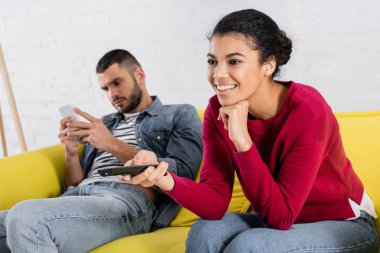 Olumlu Afrikalı Amerikalı kadın akıllı telefonlu bulanık erkek arkadaşının yanında kanalları tıklatıyor. 