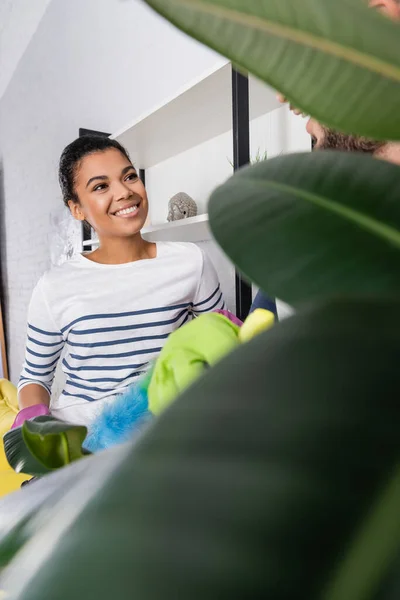 Smiling African American Woman Dust Brush Looking Boyfriend Blurred Plant — Stock Photo, Image