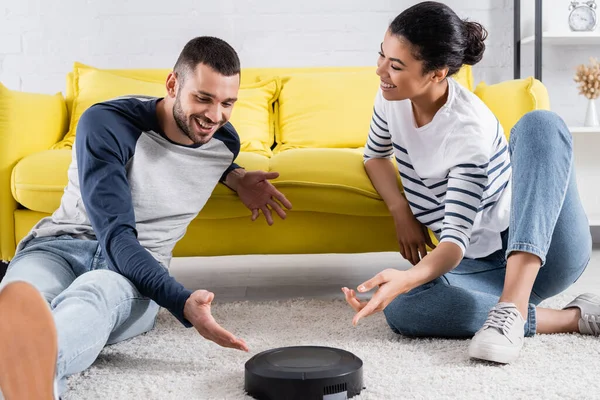 Sonriente Pareja Interracial Apuntando Aspiradora Robótica Alfombra — Foto de Stock