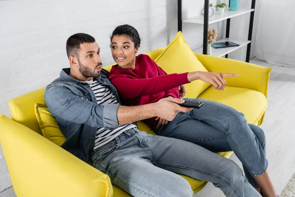 Smiling African American Woman Pointing Finger Amazed Boyfriend Remote Controller — Stock Photo, Image