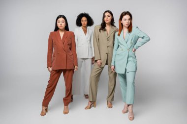 Pastel renkli takım elbiseli çok ırklı modellerin tam uzunluğu gri üzerine poz veriyor