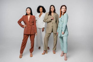 Pastel renkli giysilerle gri üzerine poz veren ırklar arası modellerin tam uzunluğu