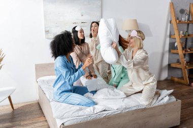 Pijamalı bir grup mutlu ırklar arası arkadaş pijama partisi sırasında yastık savaşı yapıyorlar. 