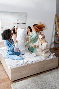 Pijamalı bir grup neşeli ırklar arası arkadaş pijama partisi sırasında yastık savaşı yapıyorlar. 