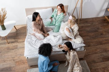 Pijama partisi sırasında konuşan neşeli çoklu etnik arkadaş grubunun yüksek açılı görüntüsü 