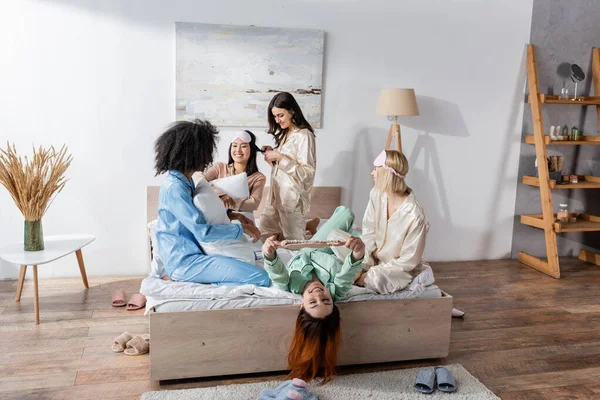スリムなパーティー中にベッドの上に座っているパジャマ姿の楽しい異人種間の友人のグループ — ストック写真