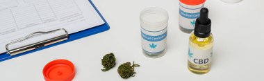 containers with oil and dry medical cannabis near clipboard on white desk, banner clipart