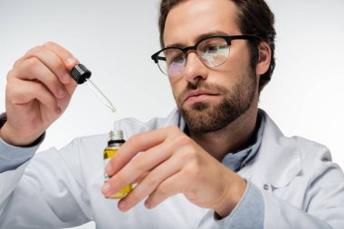 Gözlüklü doktor elinde damlatıcı ve beyaz üzerine izole edilmiş bir şişe cbd yağı tutuyor.