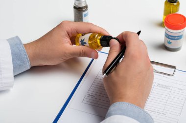 Bir şişe tıbbi kenevir yağıyla reçeteli panonun yanındaki doktorun kısmi görüntüsü