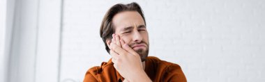man touching cheek while suffering from toothache at home, banner clipart