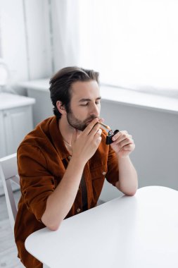 Evde tıbbi esrar içerken elinde çakmak tutan bir adam 