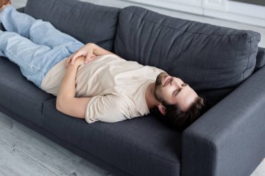 Tired man suffering from stomachache on couch clipart