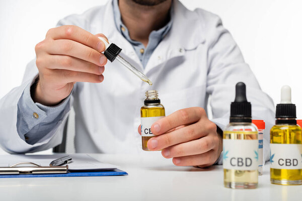 partial view of doctor holding dropper and vial with cbd oil isolated on white