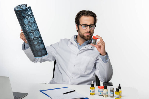 серьезный врач с МРТ и контейнер сухой медицинской марихуаны изолированы на белом