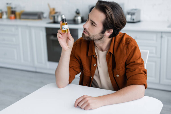 Мужчина смотрит на бутылку масла CBD дома 
