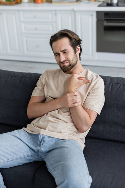 Man touching arm while feeling pain at home 