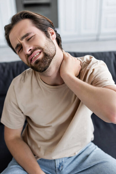 Tired man touching painful neck at home 